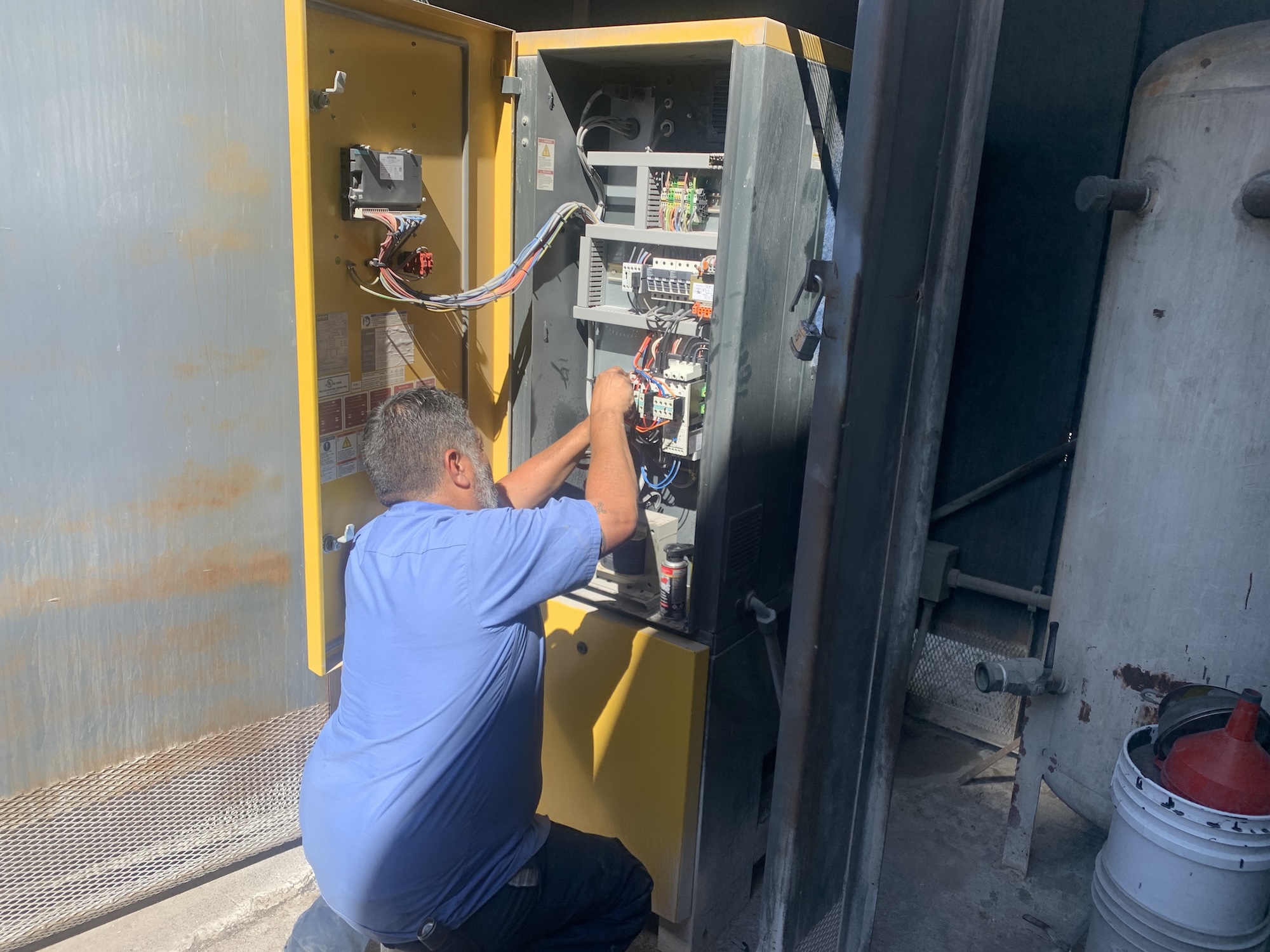 American Compressor technician performing preventative maintenance on a rotary screw compressor control panel